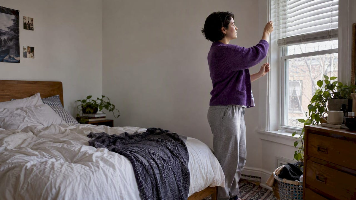 Woman opening bedroom blinds in morning light